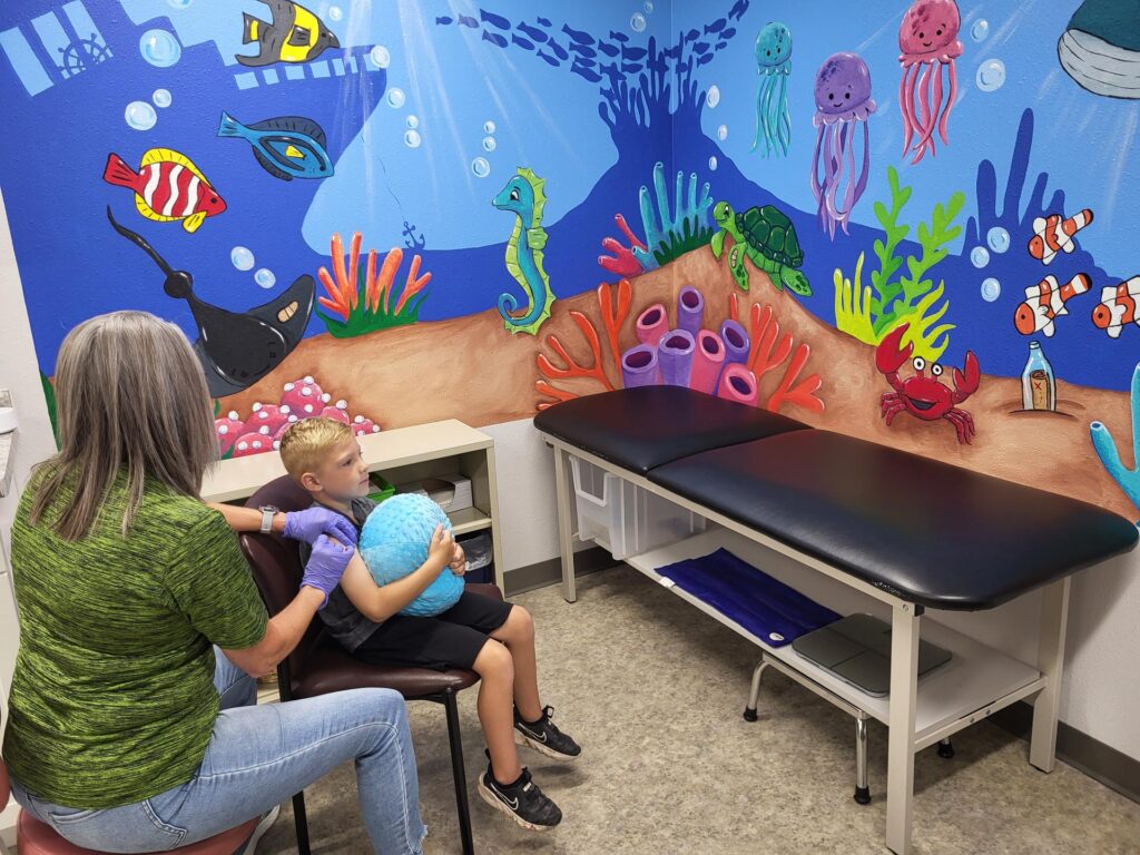 A child receiving a shot in Public Health's clinic with an underwater mural painted on two walls.